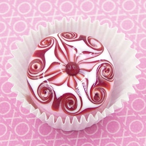 May include: A white and pink candy with a swirl design and a red center, sitting in a white paper cupcake liner.