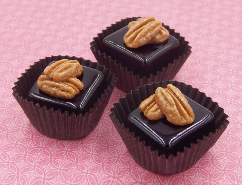 Puede incluir: Tres caramelos de chocolate y nuez pecana en vasos de papel individuales. Cada caramelo es un cuadrado de chocolate negro cubierto con mitades de nuez pecana.