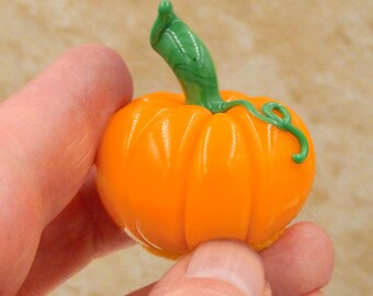 May include: A small, hand-blown glass pumpkin with a green stem and a swirl pattern. The pumpkin is orange and has a glossy finish.