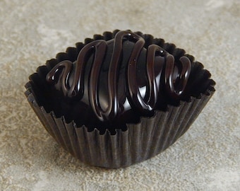 May include: A single dark chocolate truffle with a swirl of chocolate on top, sitting in a black paper cup.