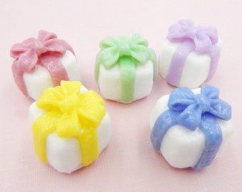 May include: Six miniature gift boxes with white frosting and colorful bows. The bows are pink, green, yellow, blue, and purple.