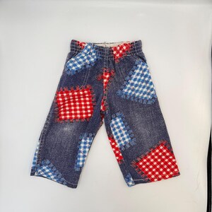 May include: Blue denim trousers with red and blue gingham patches. The patches are sewn onto the trousers with visible stitching. The trousers have an elasticated waistband.