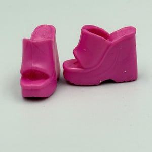 Puede incluir: Un par de sandalias de cuña de color rosa brillante. Los zapatos de punta abierta tienen una suela de plataforma y un tacón de cuña. Las sandalias están hechas de un material liso y sólido. Los zapatos están diseñados para ser usados como accesorio de moda.