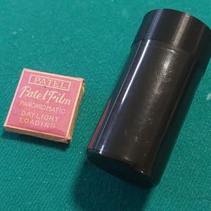 Może przedstawiać: Różowe i białe pudełko z napisem "Patel Film Panchromatic Daylight Loading" i czarny plastikowy pojemnik.