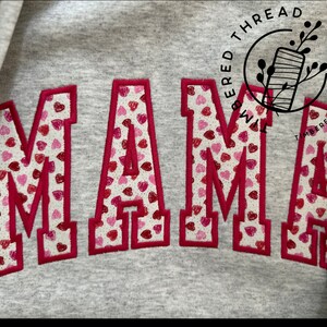 May include: A gray sweatshirt with the word "MAMA" embroidered in red with a pattern of small pink and red hearts.