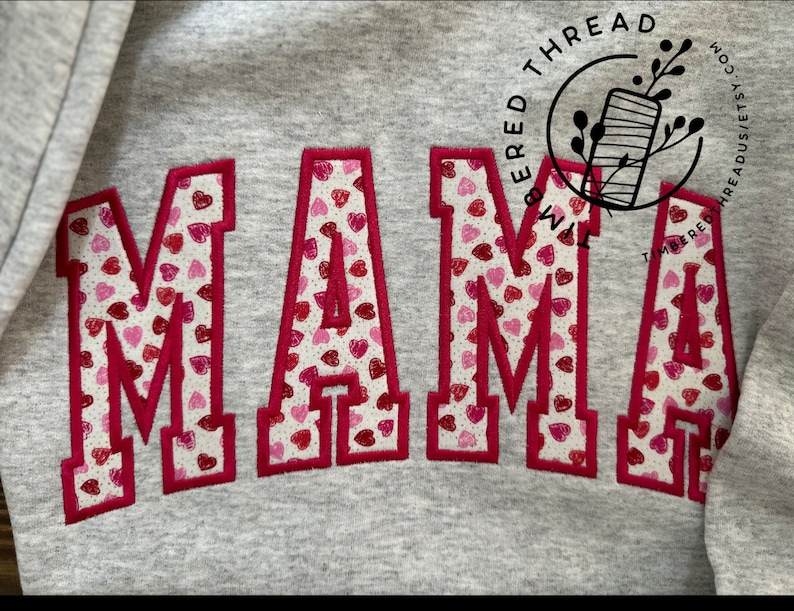 May include: A gray sweatshirt with the word "MAMA" embroidered in red with a pattern of small pink and red hearts.