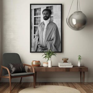 Puede incluir: Fotograf&iacute;a en blanco y negro de un hombre con una t&uacute;nica. El hombre est&aacute; de pie frente a un edificio con ventanas. La fotograf&iacute;a est&aacute; enmarcada en un marco negro.