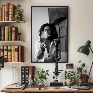 Pu&ograve; includere: Fotografia in bianco e nero di un uomo con i dreadlocks che fuma una sigaretta. L'uomo indossa una camicia bianca e guarda la fotocamera. Lo sfondo &egrave; un'immagine sfocata di un albero.