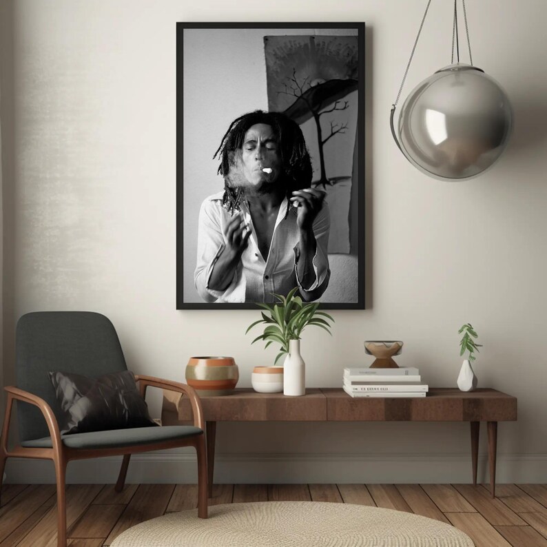 Pu&ograve; includere: Fotografia in bianco e nero di un uomo con i capelli lunghi che fuma una sigaretta. La foto &egrave; incorniciata da una cornice nera e appesa a un muro bianco. C'&egrave; un tavolo di legno con un vaso di piante e un libro sopra.