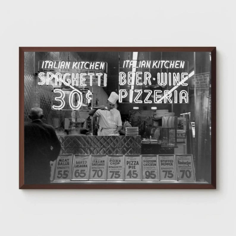 May include: A monochrome image of an Italian restaurant. Neon signs advertise "Italian Kitchen," "Spaghetti 30p," "Beer-Wine," and "Pizzeria." A chef is visible behind the counter. Menu items include spaghetti, pizza, and stuffed peppers.