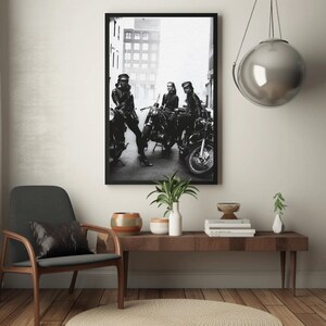 May include: Black and white framed photograph featuring three people posing with motorcycles. The image is a vintage-style print, with the subjects wearing leather jackets and hats. The photograph is displayed above a wooden console table.