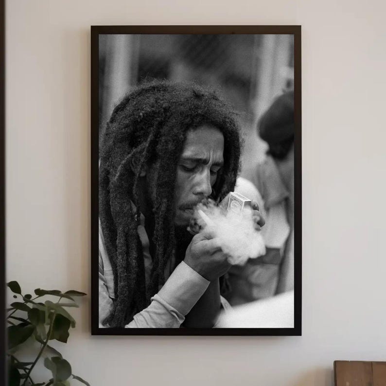 Pu&ograve; includere: Foto in bianco e nero di un uomo con lunghi dreadlocks che fuma una pipa. Indossa una camicia bianca e ha un'espressione seria sul viso.