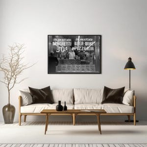 May include: Monochrome framed print of an Italian restaurant storefront. The sign reads "Spaghetti 30&cent;" and "Beer-Wine Pizzeria." A sofa with brown cushions and a wooden coffee table are in front of the print.