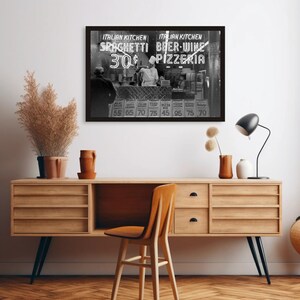 May include: Black and white framed photograph of an Italian restaurant storefront. The neon sign reads "Spaghetti" and "Beer-Wine Pizzeria". A person in a chef's hat is visible behind the counter. The photograph is mounted above a wooden cabinet.