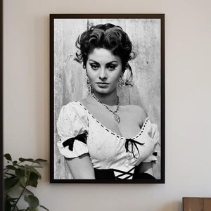 May include: Black and white portrait photograph of a woman with dark hair styled in a bouffant. She is wearing a white blouse with black accents and a necklace with a pendant.