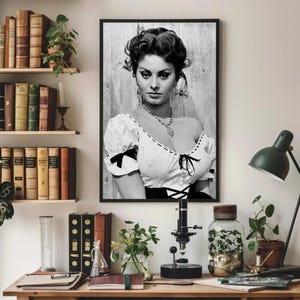 May include: Black and white portrait photograph of a woman with dark hair styled in a bouffant. She is wearing a white blouse with a lace neckline and a black bodice. The woman is looking directly at the camera with a serious expression.