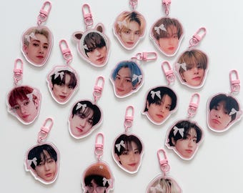 May include: A set of 16 clear acrylic keychains featuring different photos of young men. Each keychain has a pink bow and a silver metal ring.