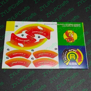 May include: A sheet of stickers featuring a red, yellow, and orange design with the text "DRANZER-S" and a blue and yellow sticker with the text "RIGHT SPIN" and the letter "R" in a circle.