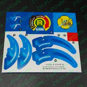 May include: A blue and yellow sticker sheet with instructions for assembling a Beyblade toy. The sheet includes a right spin symbol, a blue and white Beyblade, and the text "DRIGER" and "ベイブレード ドライガーS".