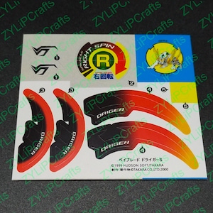 May include: A sheet of stickers for a Beyblade toy. The stickers are red, black, and yellow. The stickers feature the words "DRIGER" and "RIGHT SPIN".