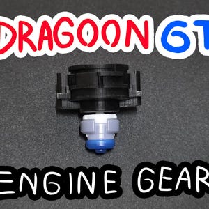 Puede incluir: Un Engine Gear negro y gris con el texto "DRAGOON GT" en rojo y azul. El engranaje tiene una base blanca, gris y azul. El producto está sobre una superficie gris oscuro.