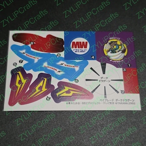 May include: A sticker sheet with various colourful stickers featuring a spinning top toy, a dragon, and a metal weight. The stickers are labelled with numbers and the text "Dark Dragoon".