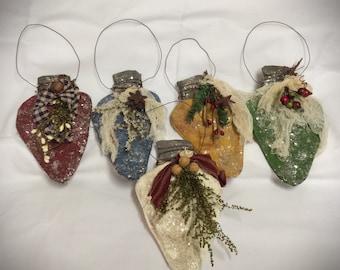 May include: Five handmade, heart-shaped Christmas ornaments in various colors: red, blue, yellow, green, and cream. Each ornament has a wire loop for hanging, a decorative top, and is embellished with fabric, berries, and greenery.