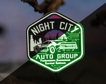 May include: A hexagonal sticker with the text "NIGHT CITY AUTO GROUP" and a car graphic. The sticker has a neon green border and accents, with a purple and pink sky background. The text "Performance Guaranteed, Survival Optional" is also included.
