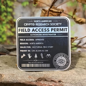 Puede incluir: Una pegatina en blanco y negro de Permiso de Acceso al Campo de la North American Cryptid Research Society. El permiso incluye detalles como "Investigador Autorizado", acceso al campo "Aprobado" y validez para "Estudio de Campo Nocturno".