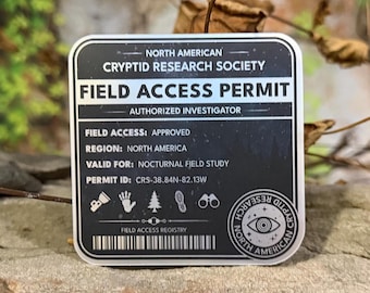 May include: A black and white Field Access Permit sticker from the North American Cryptid Research Society. The permit includes details like "Authorized Investigator," "Approved" field access, and "Nocturnal Field Study" validity. The sticker is on a rock.