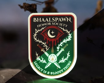 May include: A sticker with the text "BHAALSPAWN HONOR SOCIETY" and the phrase "LEGACY IS A BLOODY THING." The sticker features a red eye with a crescent moon, crossed swords, and a green and white design. Two dice are in the background.