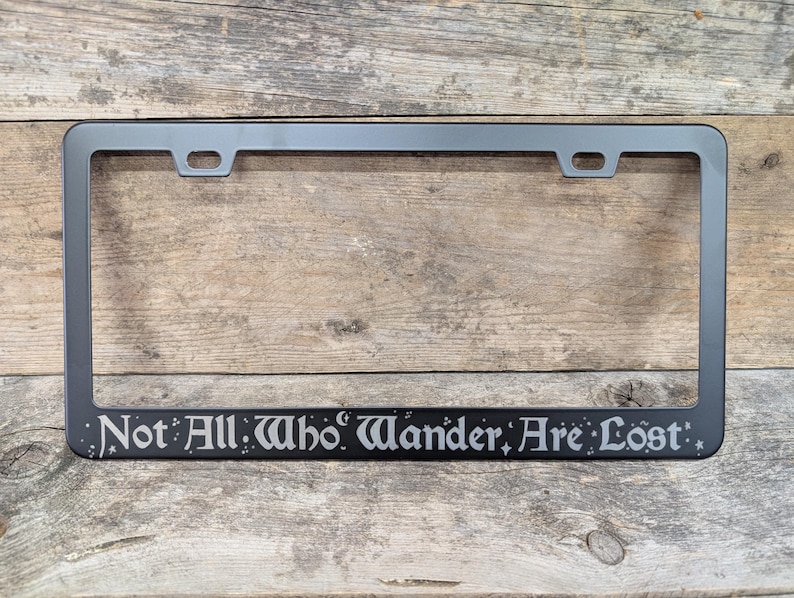 May include: Black metal license plate frame with the quote "Not All Who Wander Are Lost" in a decorative font.