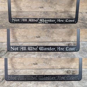 May include: Black metal license plate frame with the quote "Not All Who Wander Are Lost" in a silver font. The quote is from J.R.R. Tolkien's The Fellowship of the Ring.