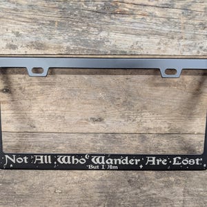 May include: Black metal license plate frame with the text "Not All Who Wander Are Lost." - But I Am.