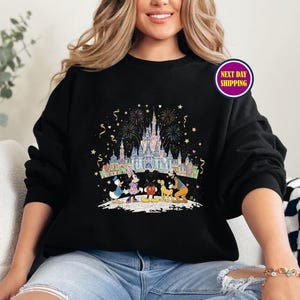 May include: Black sweatshirt featuring a colorful illustration of a castle, fireworks, and cartoon characters. The design includes Donald Duck, Mickey Mouse, and Minnie Mouse. The sweatshirt has a crew neck and long sleeves.