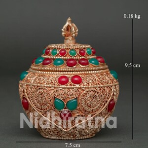May include: A round, metallic lidded container featuring intricate filigree patterns, adorned with inlaid red and green cabochon stones. The vessel has a finial on the lid, measures 9.5 cm in height, 7.5 cm in width, and weighs 0.18 kg.