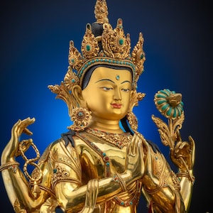 Könnte beinhalten: Eine goldene Statue einer Gottheit mit aufwendigen Details. Die Figur trägt eine juwelenbesetzte Krone und hält eine Blume. Die Statue hat einen ruhigen Ausdruck und ist mit türkisen und roten Akzenten verziert. Der Hintergrund ist ein Blauton.