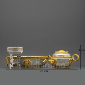 May include: A silver and gold-toned decorative set, featuring a serving dish and a lidded container. The set is approximately 24 cm long and 11 cm tall. The design includes ornate detailing and the text "Nidhiratna".
