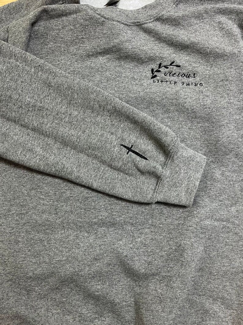 Op de afbeelding: Een grijze gem&ecirc;leerde sweatshirt met de in zwart geborduurde tekst "vicious little thing" op de borst. Een zwart zwaard is geborduurd op de linkermouw. De sweatshirt heeft een ronde hals en lange mouwen.