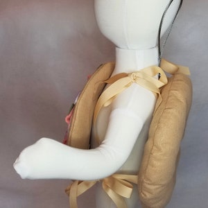 K&ouml;nnte beinhalten: Ein gepolsterter Rucksack aus Stoff in Tan-Farbe mit einem cremefarbenen Riemen. Der Rucksack wird von einem wei&szlig;en Mannequin getragen.