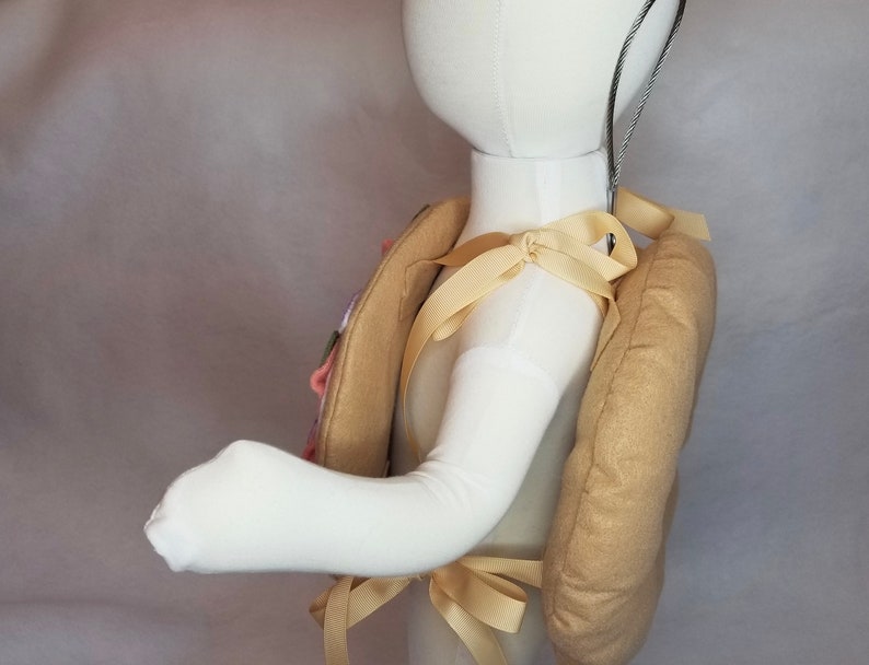 K&ouml;nnte beinhalten: Ein gepolsterter Rucksack aus Stoff in Tan-Farbe mit einem cremefarbenen Riemen. Der Rucksack wird von einem wei&szlig;en Mannequin getragen.