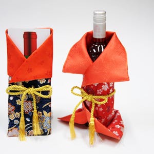 以下が含まれることがあります： 2つの装飾的なワインボトルの包み紙。1つは、金色のリボンとオレンジ色のトップが付いた濃いネイビーブルーの花柄です。もう1つは、オレンジ色のトップと金色のリボンが付いた赤い花柄です。中にはワインボトルが入っています。