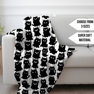 Könnte beinhalten: Eine weiße Decke mit einem sich wiederholenden Muster aus schwarzen Cartoon-Katzen. Die Decke ist über ein weißes Sofa drapiert. Auf der Seite steht "Wählen Sie aus 3 Größen" und "Superweiches Material".