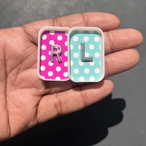 May include: Two small, rectangular, white-rimmed trays, each with a polka dot background. One has a pink background with white dots and the letter "R". The other has a teal background with white dots and the letter "L".