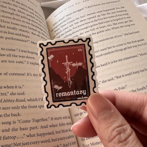 May include: A red and white sticker with a sword and the word "romantasy" in a vintage font. The sticker is shaped like a postage stamp with a 10c price tag.