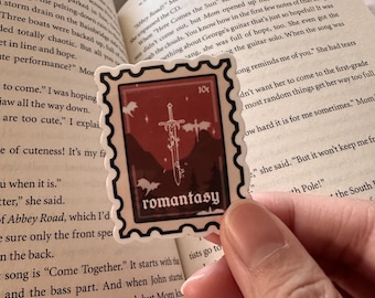 May include: A red and white sticker with a sword and the word "romantasy" in a vintage font. The sticker is shaped like a postage stamp with a 10c price tag.