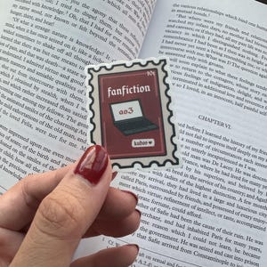 May include: A red and white sticker with the word "fanfiction" and a laptop icon. The sticker is 10 pence and has the words "a03" and "kudos" on it.