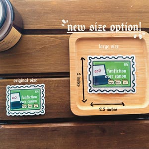 May include: Two versions of a sticker with a green background and white border. The sticker features a computer screen with the text "a03 fanfiction over canon" and the words "angst", "fluff", and "au" written below the screen. The sticker on the left is the original size, and the sticker on the right is the new larger size, measuring 2.5 inches by 2 inches.