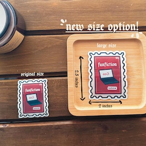 May include: Two sticker designs of a laptop with the text "fanfiction" and "a03" on a red background. The smaller sticker is 2 inches by 2.5 inches and the larger sticker is 2 inches by 2.5 inches.