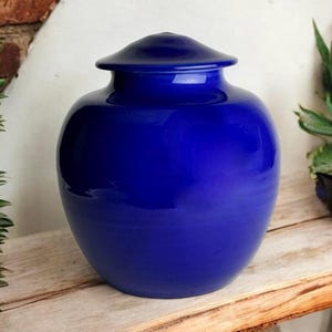 Puede incluir: Una urna de cerámica azul cobalto con tapa. La urna tiene un acabado liso y brillante.